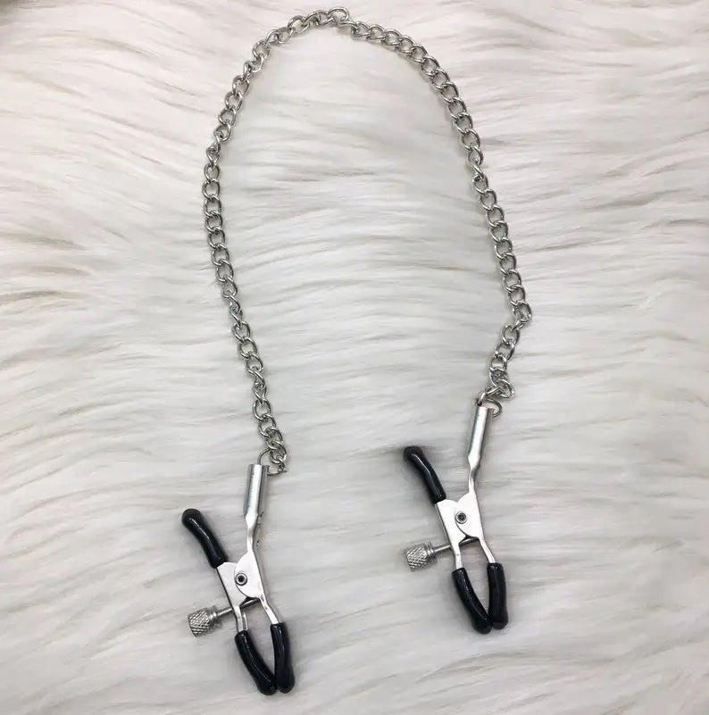 Black nipple clamps with chain on a soft white rug